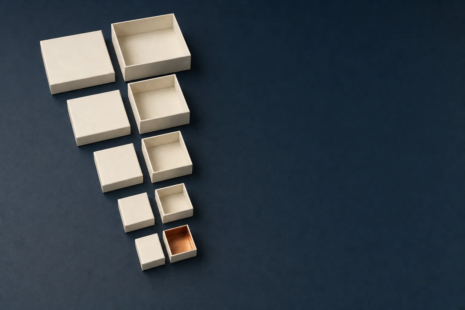 Five nested ivory boxes taken apart on a navy desk surface, each lid set beside its base, with the smallest box lined in copper