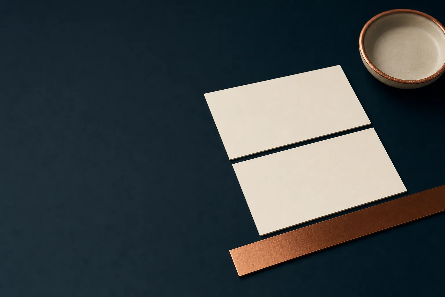 Two blank ivory business cards laid on a dark navy table beside a copper straightedge